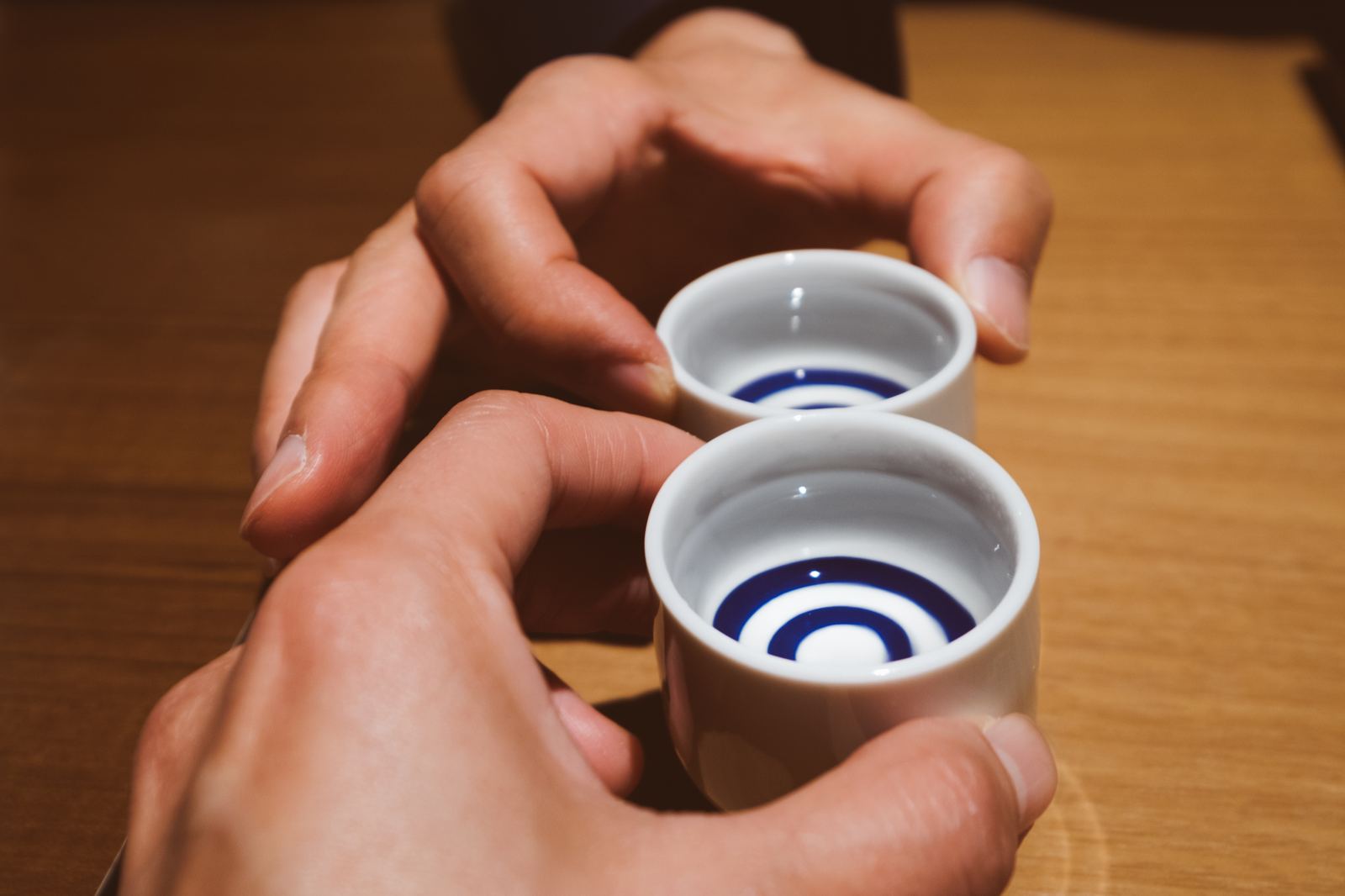 Two hands raising blue-ringed sake cups in a toast